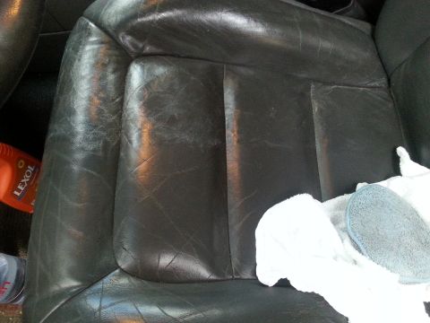 2001 Ford Explorer - A close-up view of a dark-colored leather car seat with visible wear and tear, alongside cleaning supplies including a bottle of Lexol and…
