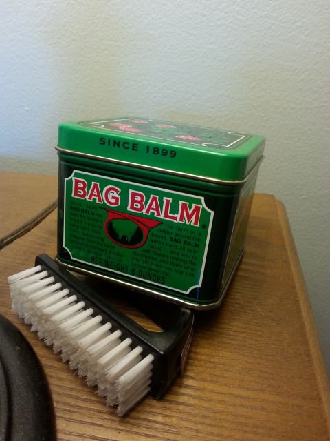 2001 Ford Explorer - A green tin of Bag Balm sits on a wooden surface next to a small brush. The tin has text and graphics on its sides and lid.
