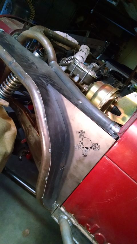 1985 Jeep CJ7 - A close-up view of the custom metalwork on a red vehicle, featuring a skull and piston emblem. The engine bay components, including a brake…
