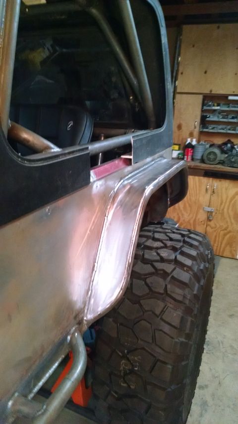 1985 Jeep CJ7 - A close-up side view of the rear quarter panel and large off-road tire of a modified Jeep CJ7. The vehicle features custom metalwork on the…
