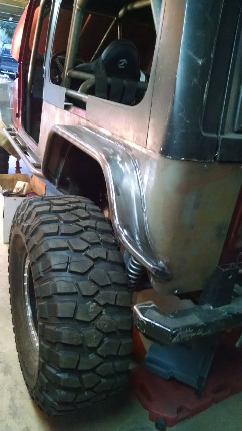 1985 Jeep CJ7 - The rear quarter panel and massive off-road tire of a custom Jeep are shown in this close-up side view. The vehicle features a roll cage an…