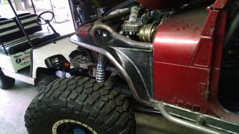1985 Jeep CJ7 - A heavily modified red Jeep CJ7 is shown next to a white golf cart. The Jeep features large off-road tires, custom metal fender flares, and…