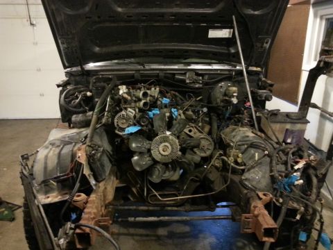 1994 Ford Bronco - The engine bay of a 1994 Ford Bronco is shown with the hood open and the engine partially disassembled. The vehicle is in a garage or works…