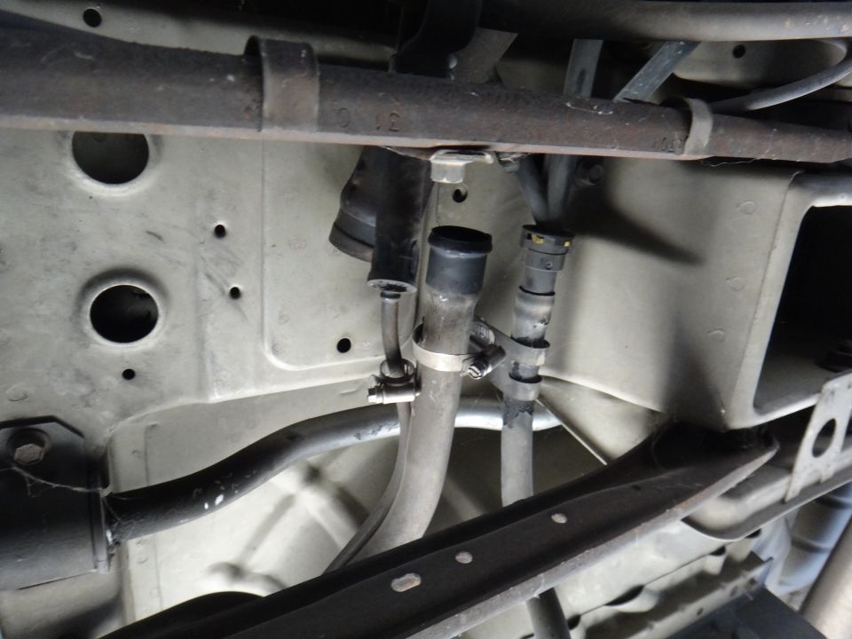 Underside of a vehicle showing metal frame, hoses, and clamps.