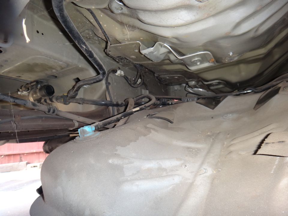 Underside of a vehicle showing fuel tank, fuel lines, and wiring.