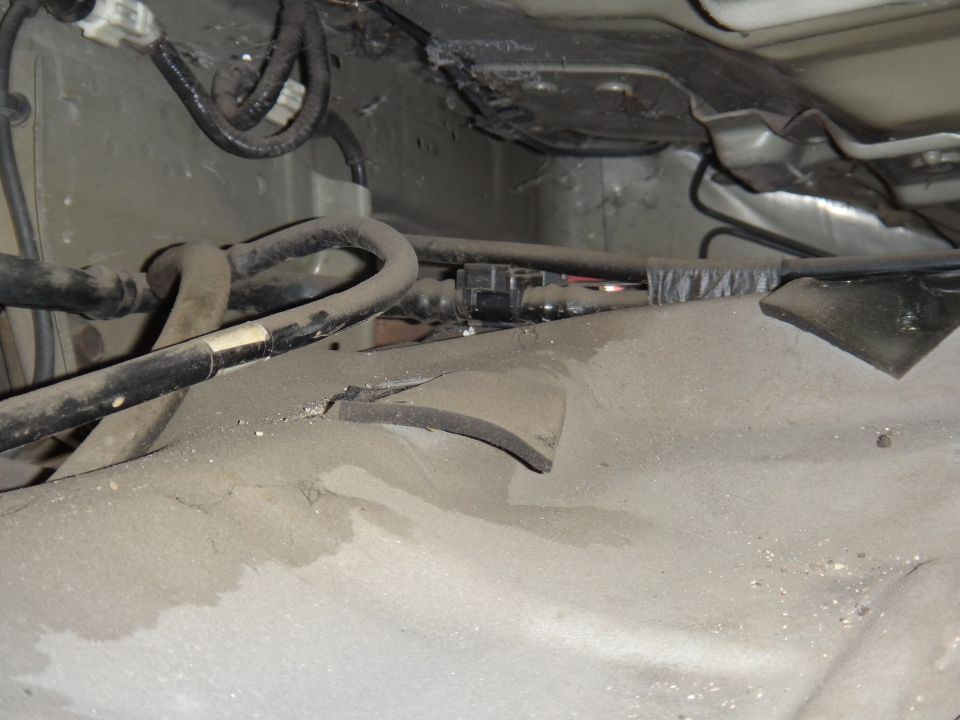 Vehicle undercarriage with fuel/brake lines and a cracked rubber cover.