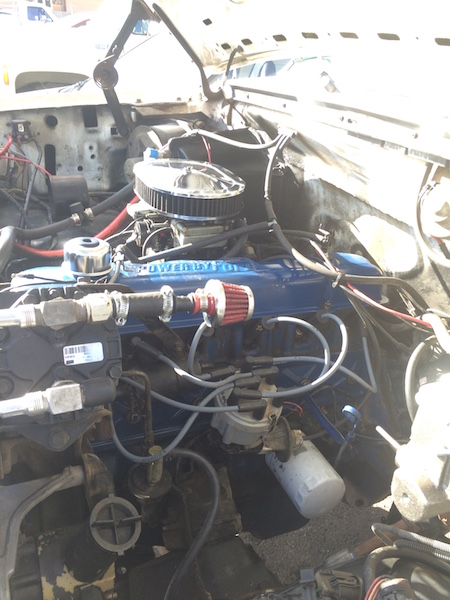 1981 Ford Bronco - The engine bay of a classic Ford Bronco, showcasing a blue Ford engine with a chrome air cleaner and various hoses and wires. A white oil f…