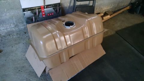 1994 Ford Bronco - A new, tan-colored fuel tank is shown resting on cardboard in a garage setting. The tank has a circular opening on top with a silver metal…