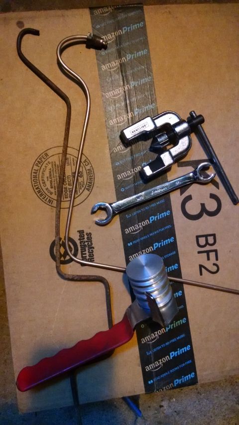 1994 Ford Bronco - A collection of automotive tools and parts are laid out on a cardboard box. Visible items include a flaring tool, a wrench, a piston, and t…