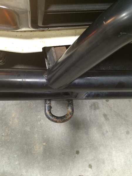 1981 Ford Bronco - A close-up view of a black metal tow hook attached to a black metal bumper on a vehicle. The tow hook shows signs of rust.