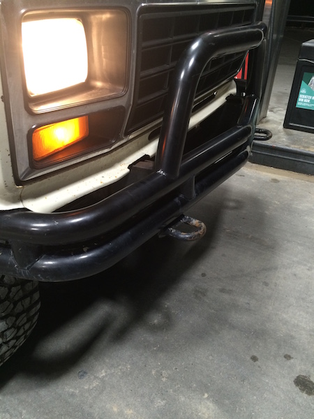 1981 Ford Bronco - Close-up front view of a white Ford Bronco with a black brush guard and a visible tow hook. The headlight and amber turn signal are illumin…