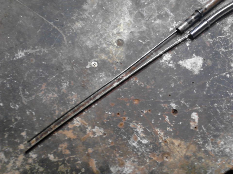 Two metal control cables on a scratched and rusty metal surface.