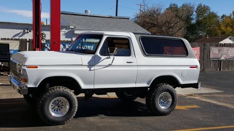 1978 Ford Bronco - A lifted, white 1978 Ford Bronco with aftermarket wheels is parked outside a building with a red lift in the foreground.
