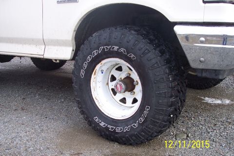 1990 Ford Bronco - A close-up shot focuses on the wheel and tire of a white pickup truck, with a "Custom" badge visible on the fender.