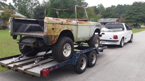1972 Ford Bronco - A heavily rusted 1972 Ford Bronco is transported on a trailer behind a white pickup truck.