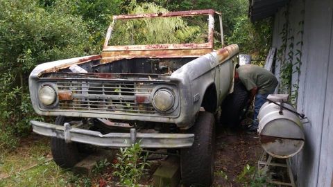 1972 Ford Bronco - A weathered 1972 Ford Bronco sits in disrepair, awaiting restoration with a person attending to its rear wheel.