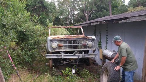 1972 Ford Bronco - A man works near a heavily rusted Ford Bronco, which appears to be a 1970s model, parked outdoors.
