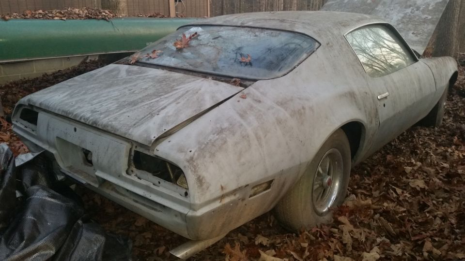 beat-up 1970s coupe with hood up, sitting in yard debris