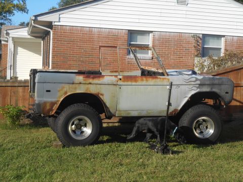 1972 Ford Bronco - A weathered 1972 Ford Bronco sits in a grassy yard next to a brick house, showing signs of restoration.