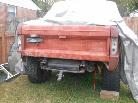 1972 Ford Bronco - Rear view of a red Ford pickup truck, showing its tailgate and taillights, partially covered by a tarp.