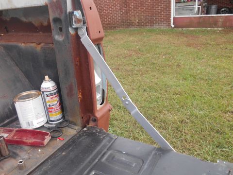 1972 Ford Bronco - A close-up view of a tailgate support arm in a rusty truck bed, alongside restoration supplies.