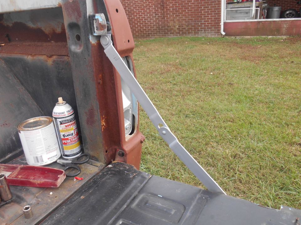 Tailgate support arm on rusty truck bed, with paint can and spray can