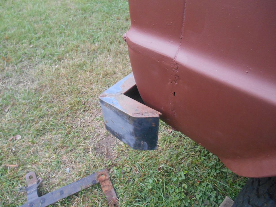 Rear corner of a vehicle with a black bumper and some rusty metal parts on the ground