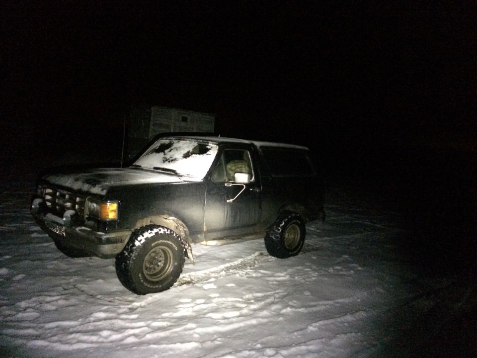 Black 1987 Ford Bronco in snow at night, front-left quarter view