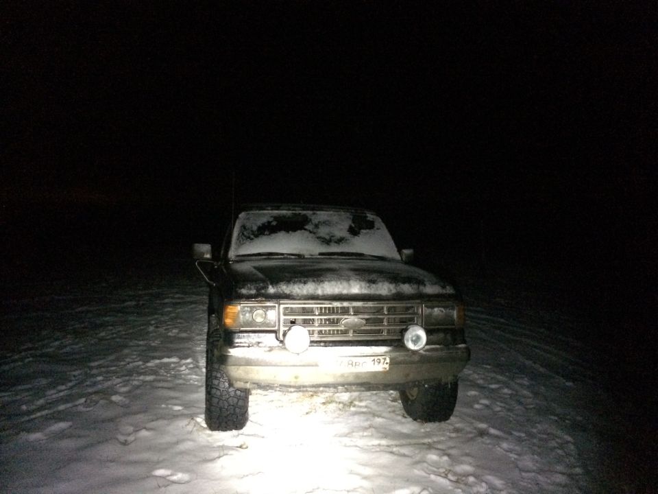 1987 Ford Bronco parked in snow at night, front view with headlights on