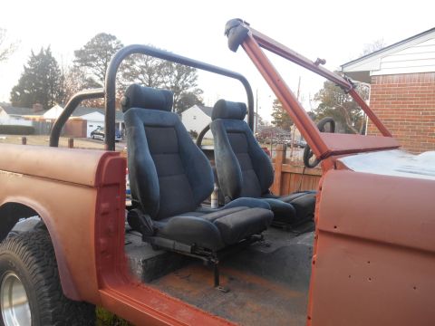 1972 Ford Bronco - The interior of a vehicle undergoing restoration shows blue bucket seats and a roll cage against a backdrop of houses.
