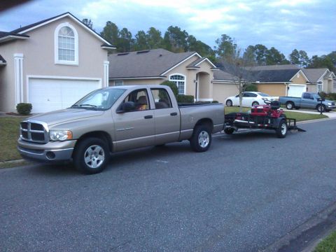 2006 Honda RANCHER - Dodge Ram pickup truck towing an ATV on a trailer down a suburban street.
