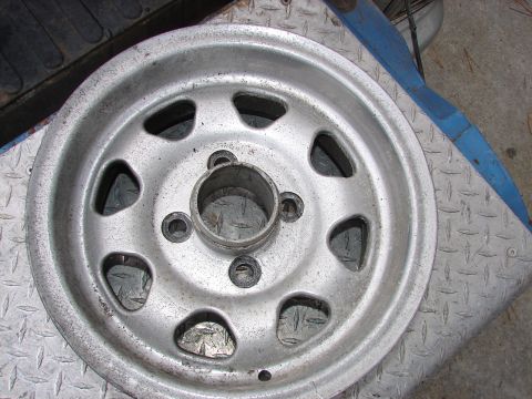 1973 Ford Ranchero - A single silver wheel with distinctive oval cutouts is shown, resting on a diamond plate surface.