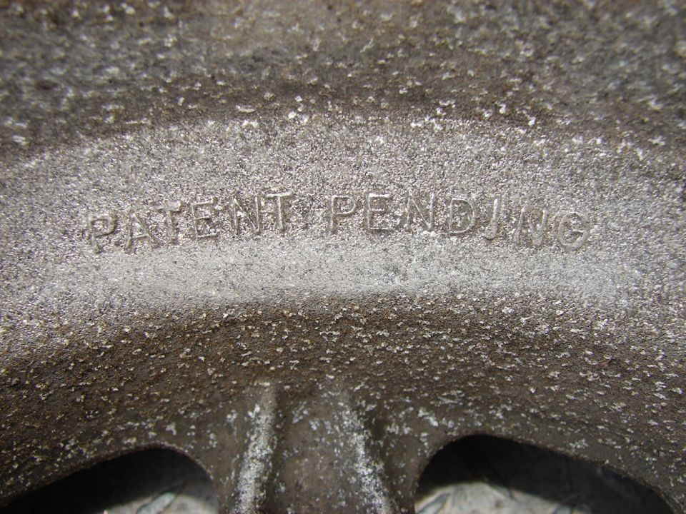 Close-up of a rough, grey metal casting with raised text reading "PATENT PENDING"