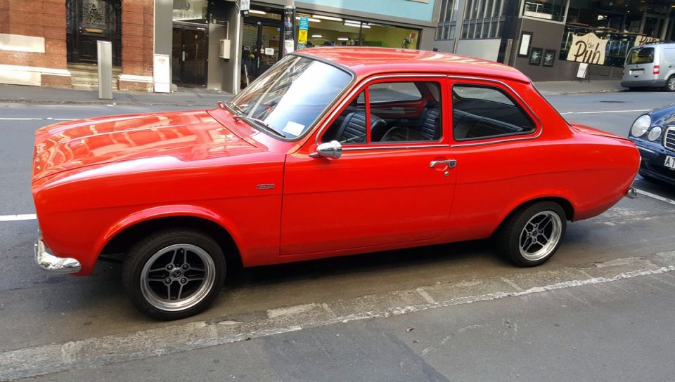 Red two-door coupe with aftermarket wheels parked on a city street