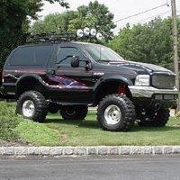 1989 Ford Bronco - This modified SUV is parked on a grassy area next to a road.