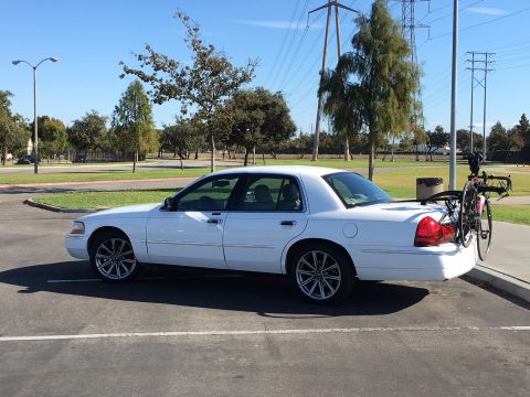 1989 Mazda MX-6 - A white sedan is parked in an outdoor lot, equipped with a bicycle rack and a bicycle on the back.