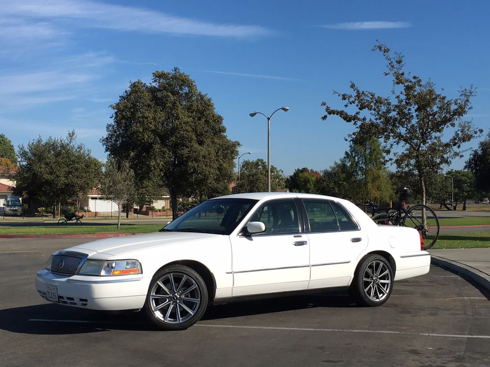 White sedan with aftermarket wheels parked outdoors. A bicycle is mounted on a rack on the rear