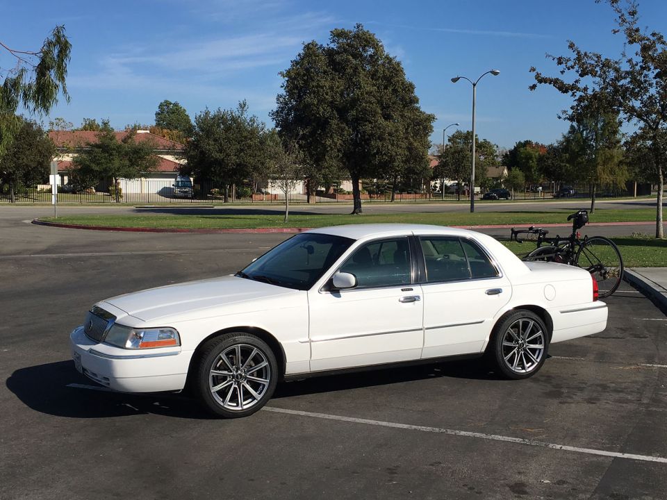 White sedan parked in a lot, side view. Bicycle rack attached to the rear