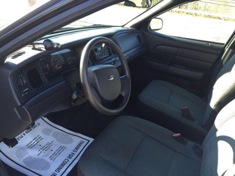 2001 Ford Crown Victoria - The interior of a police car, a dashboard, steering wheel, and front seats, with a floor mat that says "Thanks for Coming In."