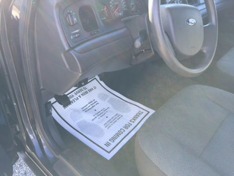 2001 Ford Crown Victoria - A floor mat with a message and footprints is placed on the driver's side floor of a car.