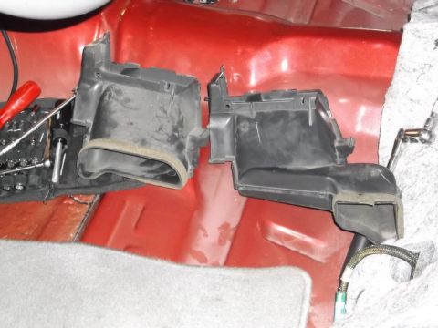 1999 Mercury Grand Marquis - Two black plastic HVAC duct pieces are disassembled and lying on the red floor of a vehicle interior. A red-handled screwdriver and a socke…