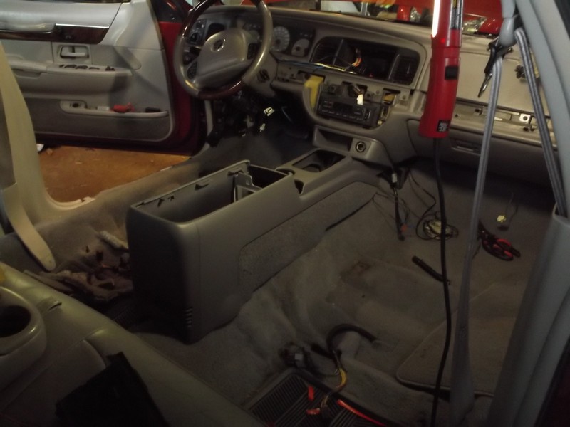 Interior of a car with dashboard and center console removed, showing wiring and tools.