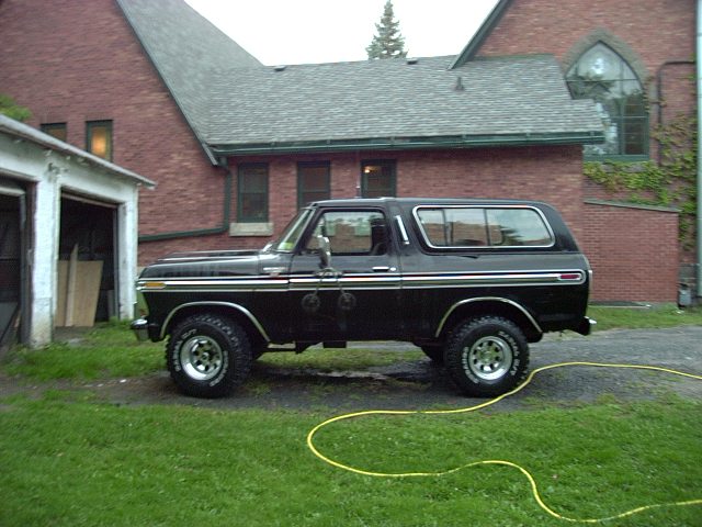 Black lifted two-door SUV parked in profile on grass by a brick house.