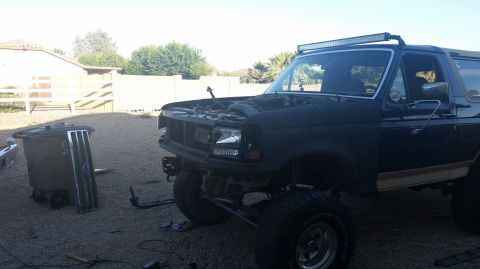 1991 Ford Bronco - A dark colored Ford Bronco with its hood open is parked in a gravel driveway. A light bar is mounted to the roof, and the front grille and…