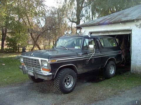 1978 Ford Bronco - A black 1978 Ford Bronco is parked outside a garage, showing its distinctive grille and side profile.