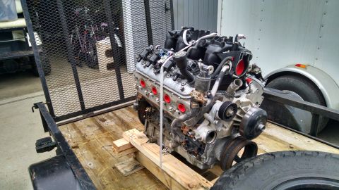 1985 Jeep CJ7 - A V8 engine is loaded onto a wooden trailer, secured with wooden blocks and straps. The engine is silver and black with red accents on the…