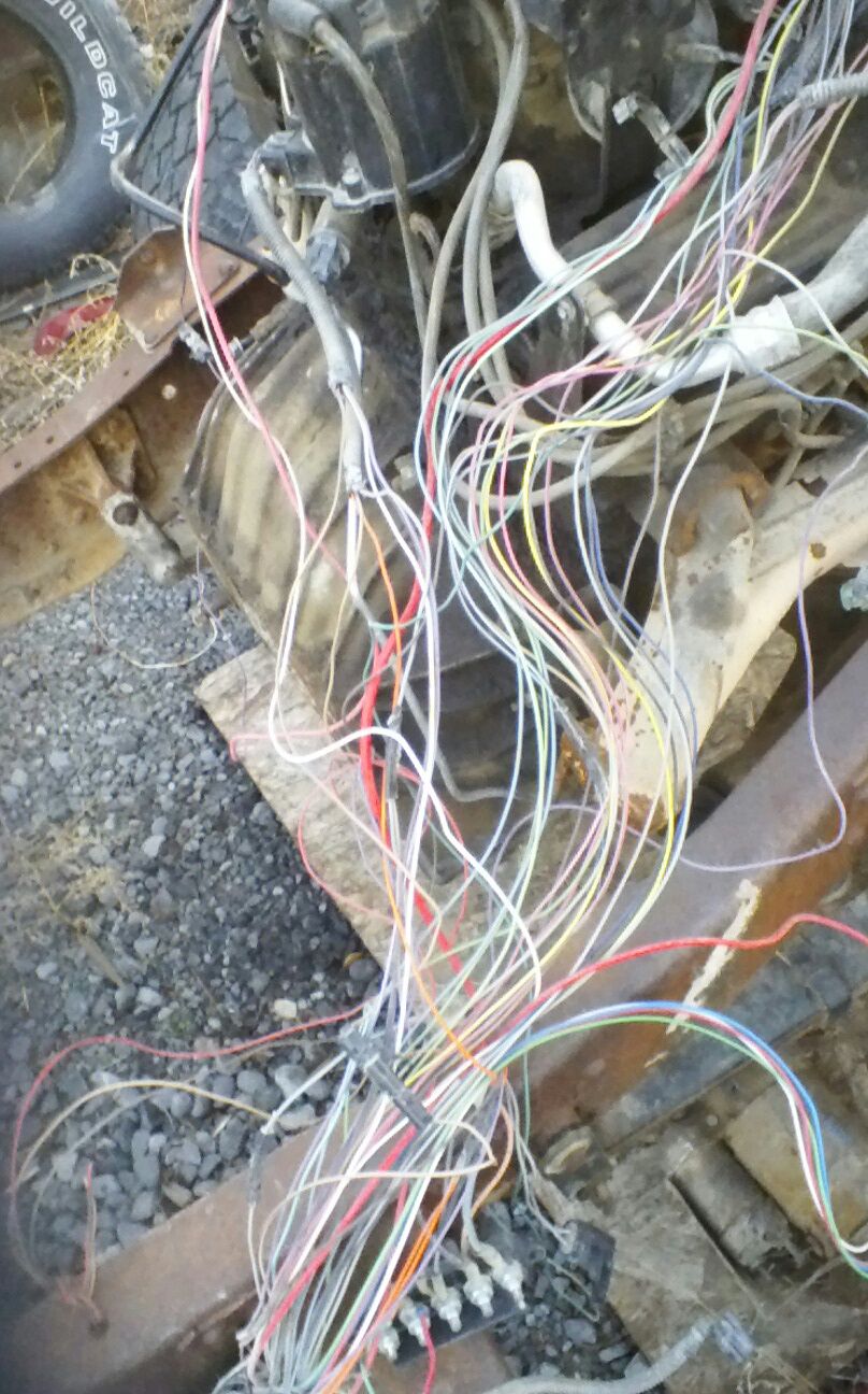 Tangled vehicle wiring harness with many colorful wires and electrical components on a rusty frame.