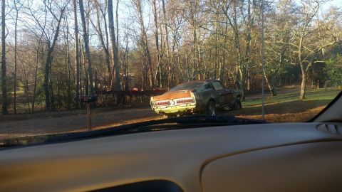 2015 Chevrolet new - A rusty, vintage green coupe is parked in a wooded area next to a mailbox. The car appears to be a Ford Mustang from the late 1960s or earl…