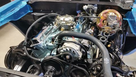 2015 Chevrolet new - A detailed view of a classic V8 engine bay, featuring a blue fender, a carburetor, an alternator, and a brake booster assembly.