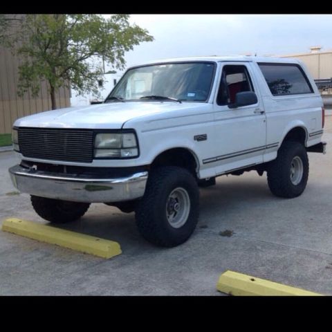 1996 Ford Bronco - A white 1990s Ford Bronco is parked on a concrete surface with yellow parking blocks in the foreground. The vehicle is shown from a 3/4 fro…